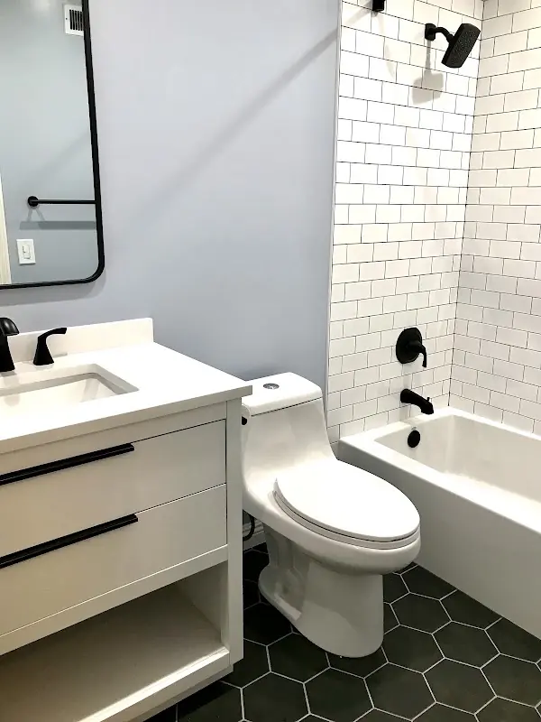 White bathtub surround with black plumbing fixtures, black hexagon floor tile, and modern vanity