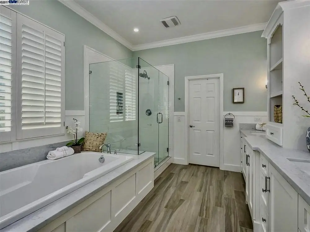 Spacious primary bathroom with glass shower, built-in tub, white cabinetry, and wood-look tile floor