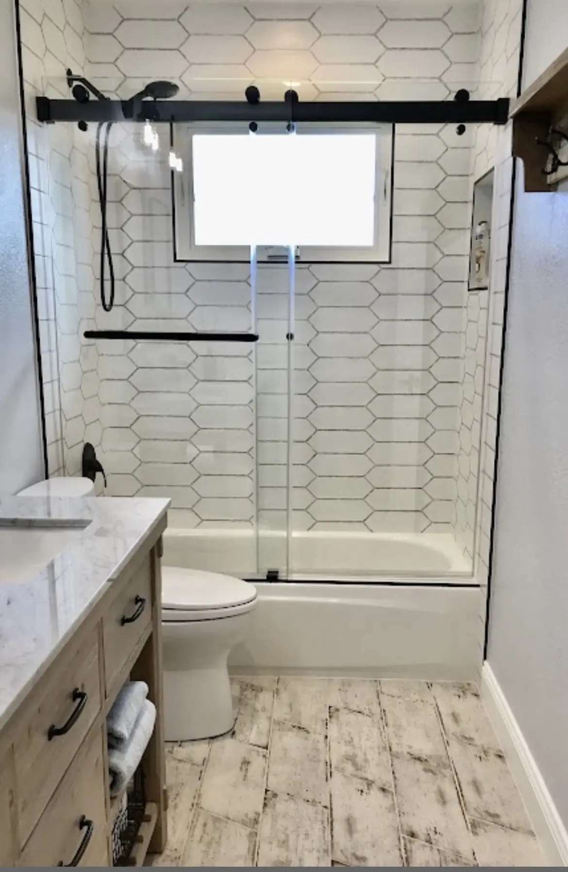 Tub and shower combination with elongated white hexagon wall tile and black sliding shower hardware