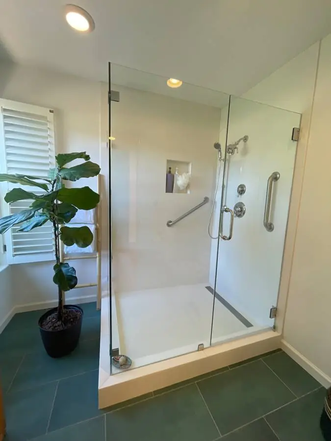Minimal frameless glass shower with large light wall tile and dark slate floor tile