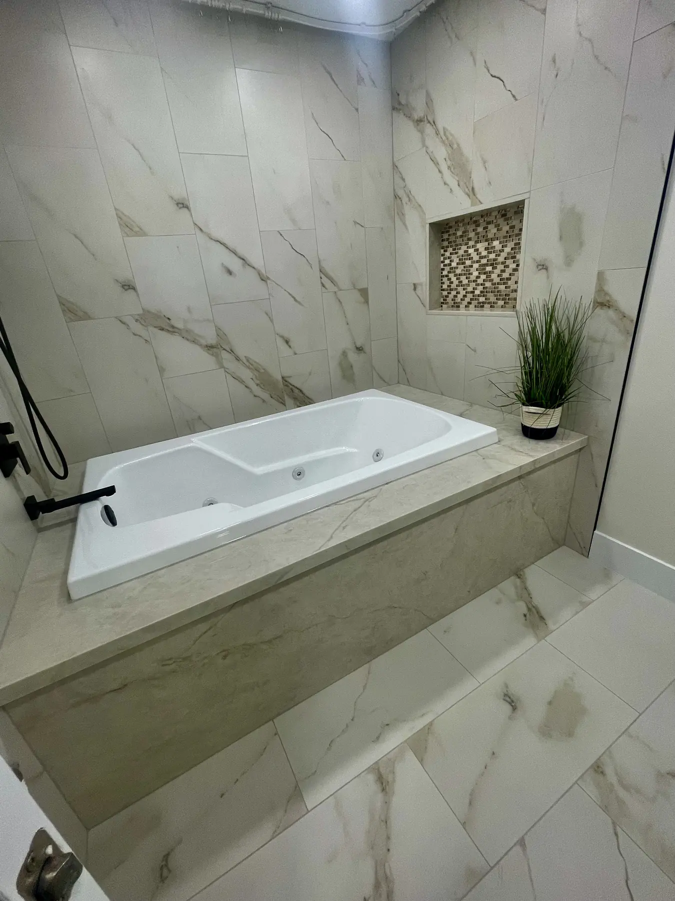 Bathtub surround finished with large-format white marble-look tile and a recessed mosaic niche