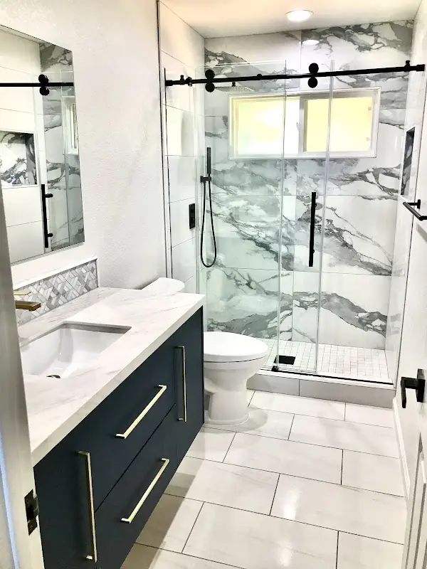 Bathroom remodel with marble-look shower walls, sliding glass doors, and navy vanity
