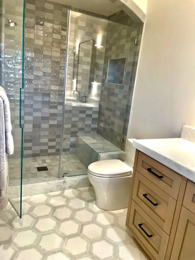 Bathroom with mosaic tile shower walls, hexagon floor tile, glass enclosure, and wood vanity