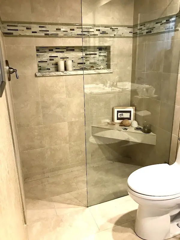 Neutral stone tile shower with glass doors, decorative mosaic band, niche, and corner bench