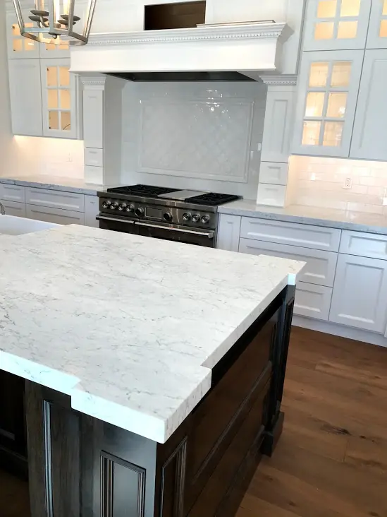 Kitchen with white stone countertops, matching backsplash, dark island cabinetry, and wood flooring