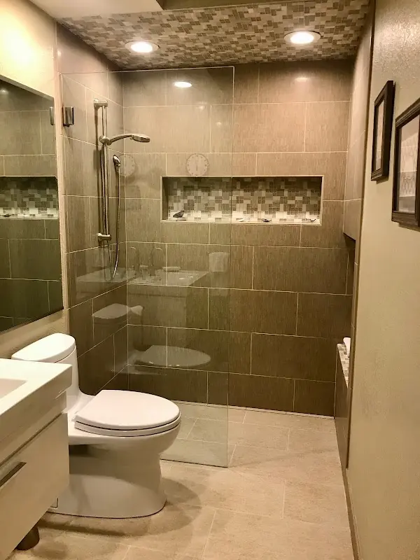 Warm stone walk-in shower with glass enclosure, recessed niche, and pebble shower floor