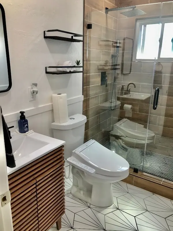 Bathroom with slatted wood vanity, glass shower, patterned floor tile, and black fixtures